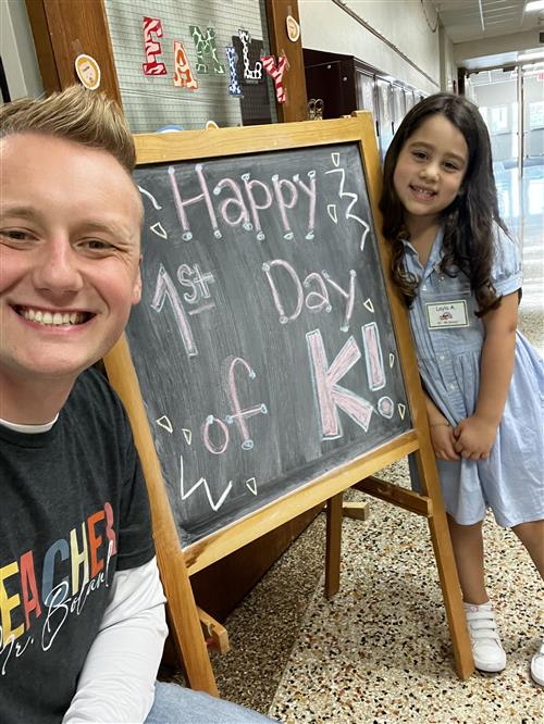 student and teacher next to "Happy First Day of K" sign
